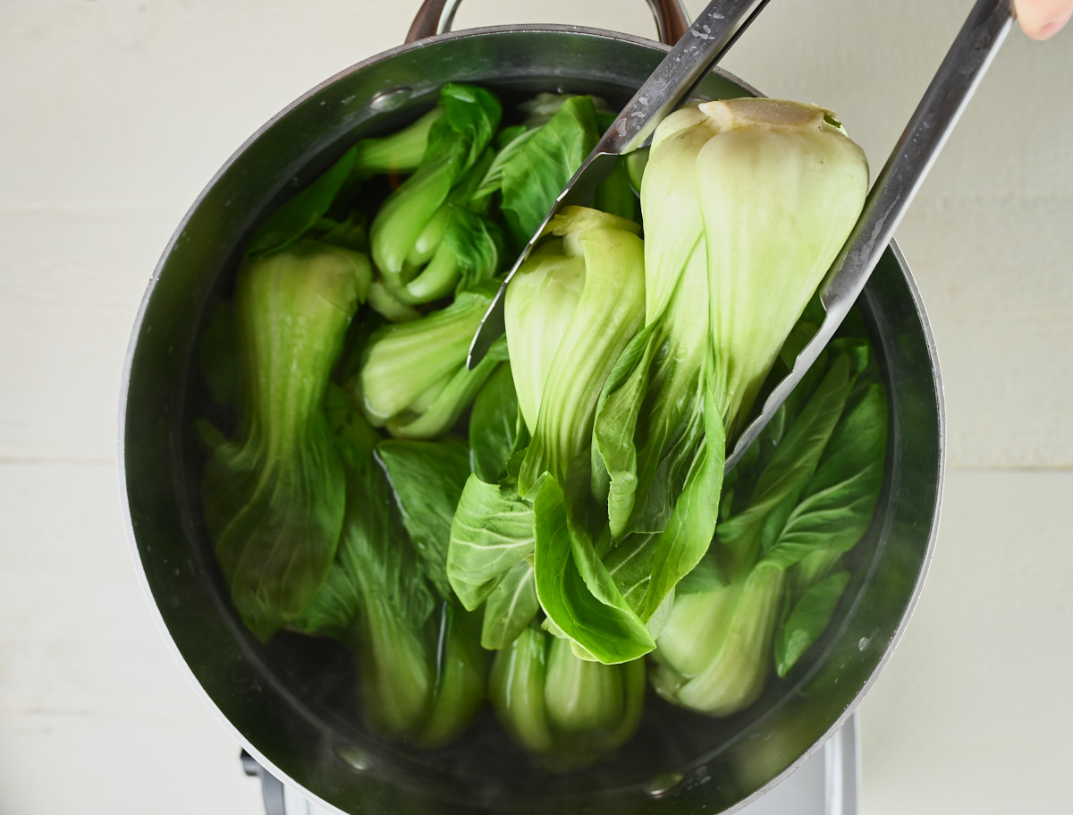 baby bok choy being put in a pot with tongs