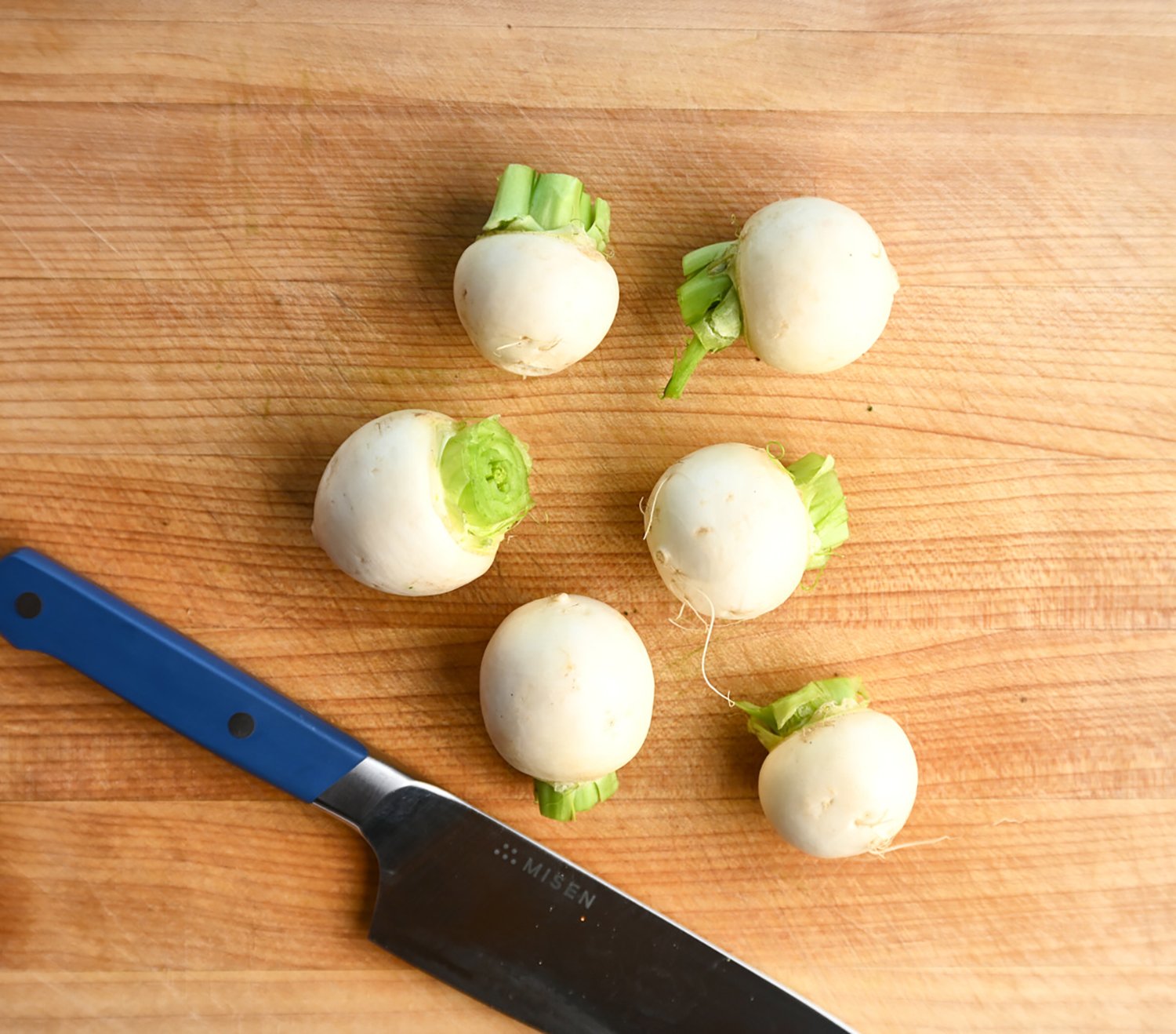 six turnip without greens on a wooden cutting board, next to a knife