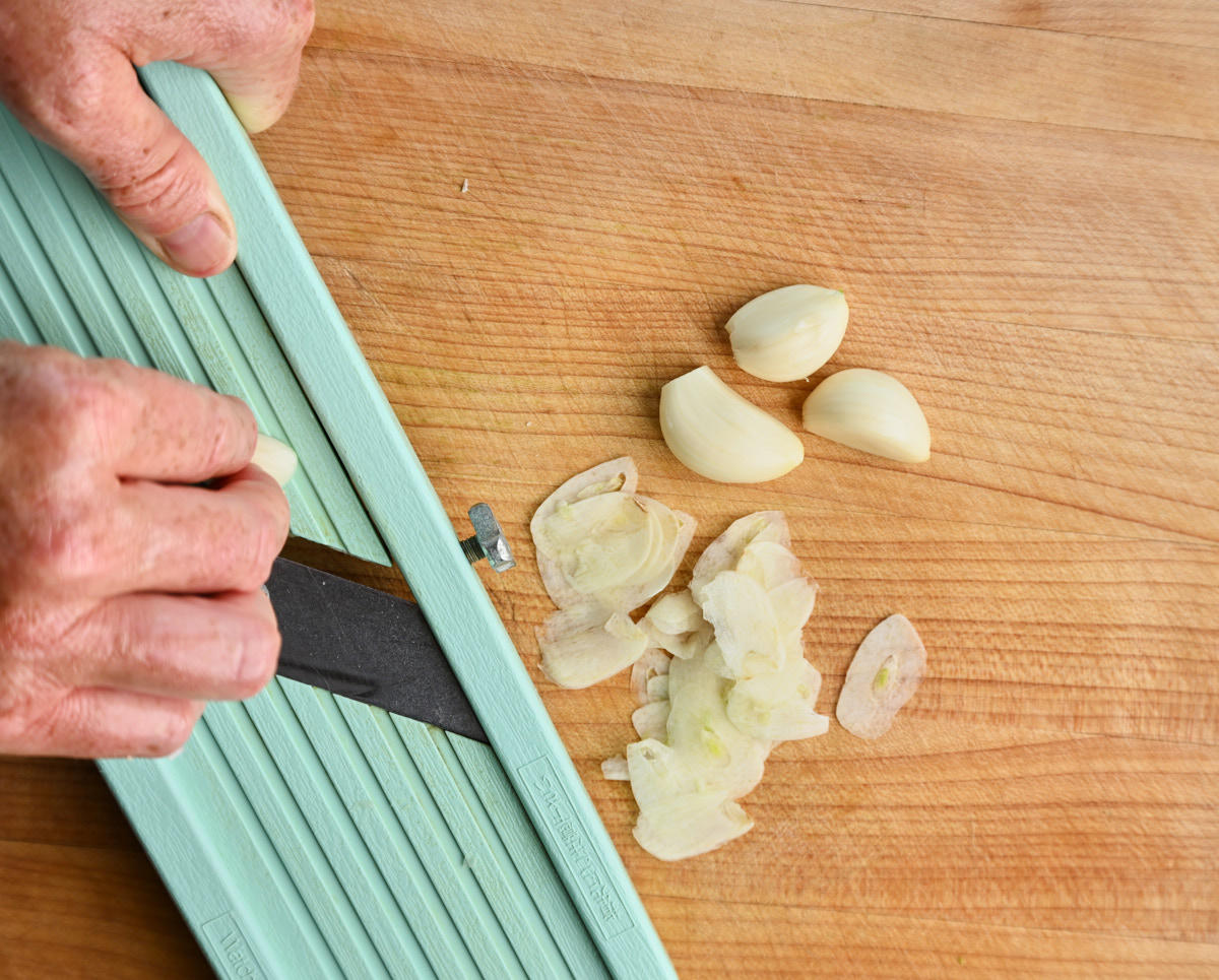 garlic cloves being sliced thinly on a mandolin