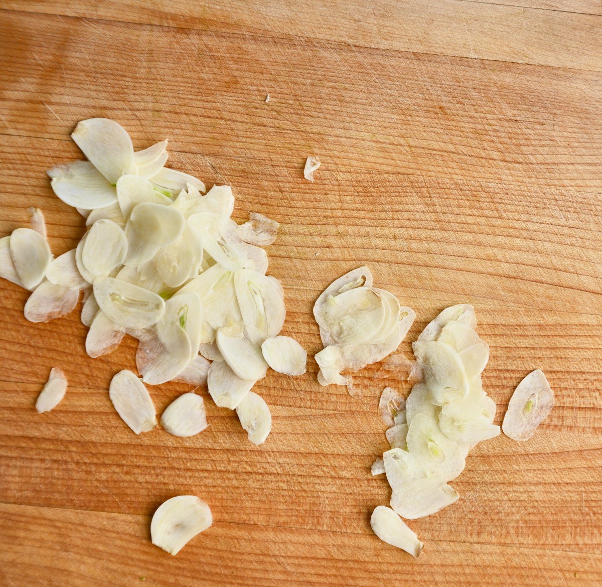 thinly sliced garlic on a wooden cutting board