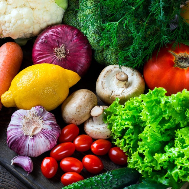 photo of produce: cherry tomatoes, mushrooms, lettuce, garlic, lemon, rosemary, cauliflower, and carrots all stacked up on one another.
