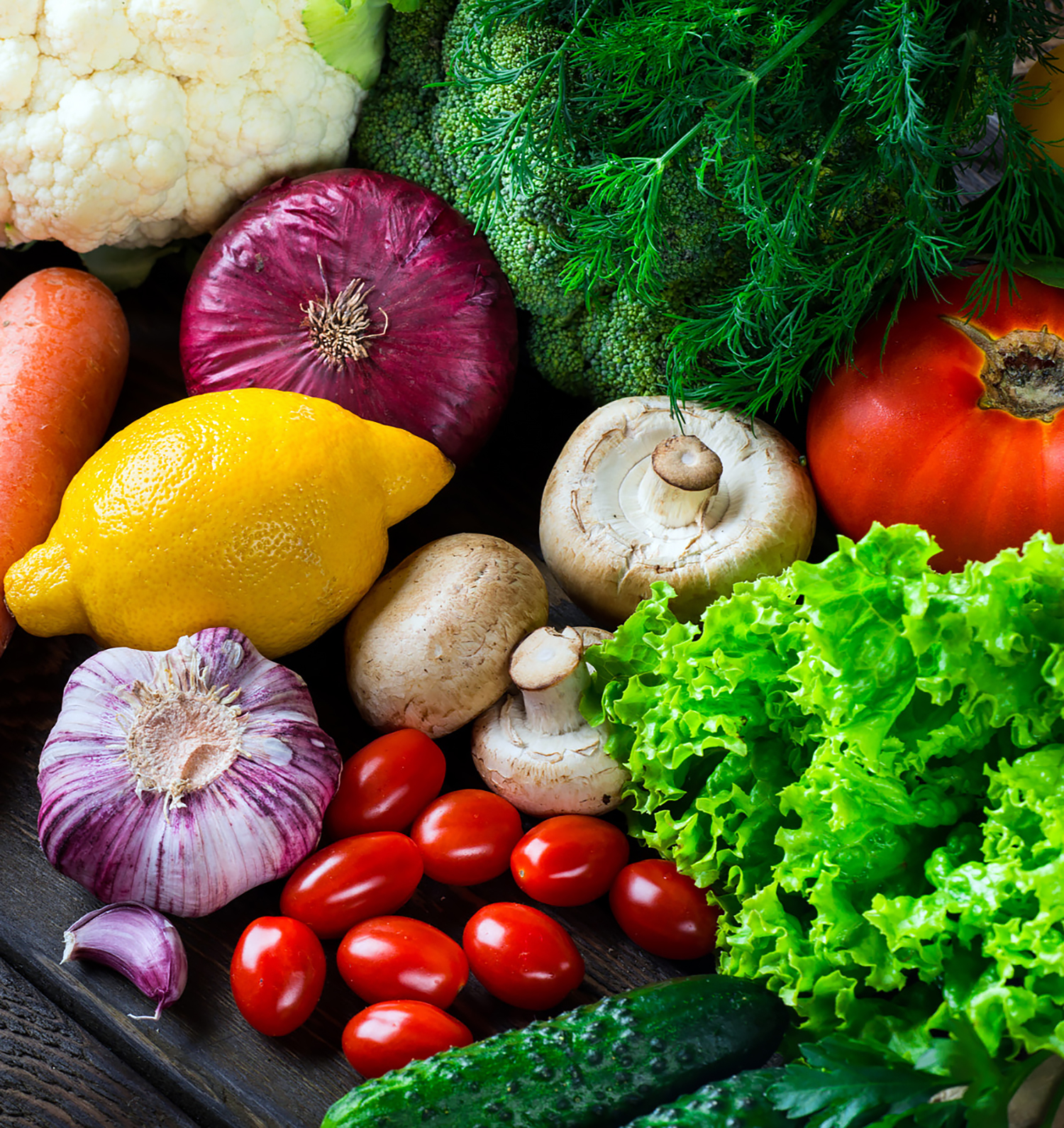 photo of produce: cherry tomatoes, mushrooms, lettuce, garlic, lemon, rosemary, cauliflower, and carrots all stacked up on one another.