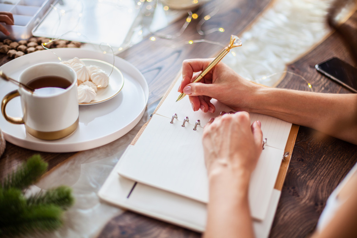 An organized women sitting at a table to write down a list in a notebook.