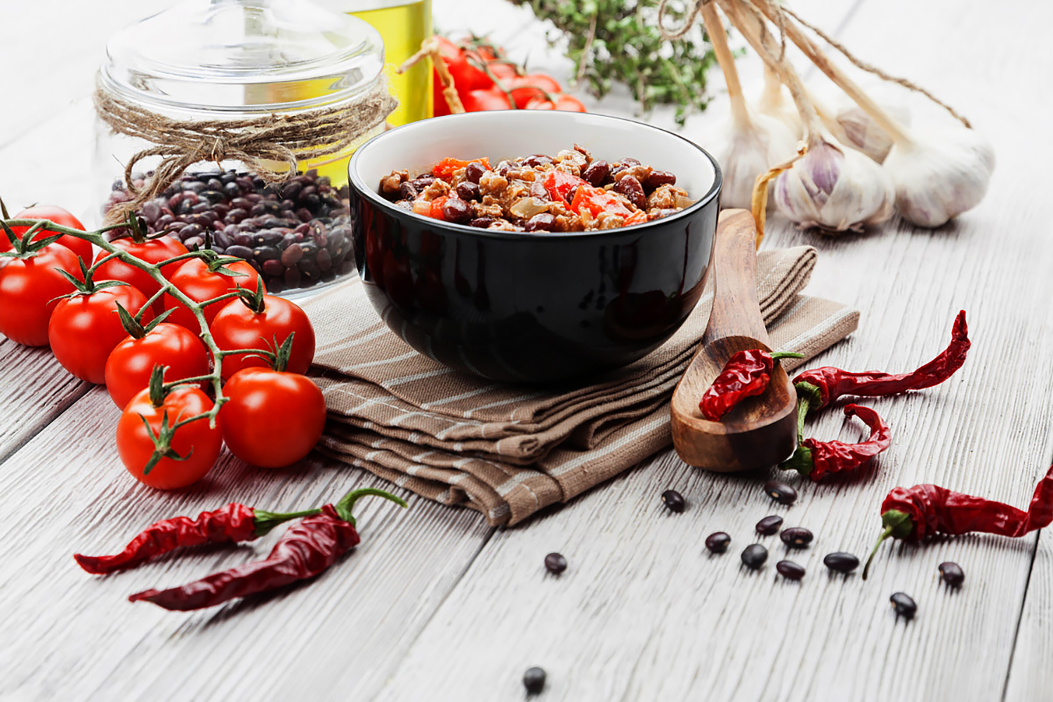 tomatoes, beans, garlic, chili peppers, olive oil on a slatted table top from a stocked pantry