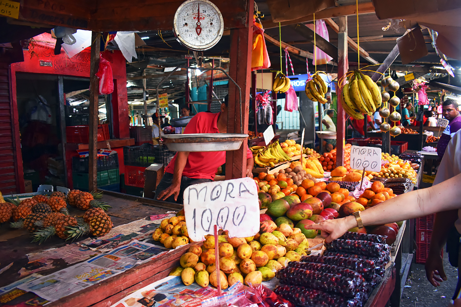 Produce market, hanging bananas, pineapples, mangos, lemons and other produce stacked and for sale