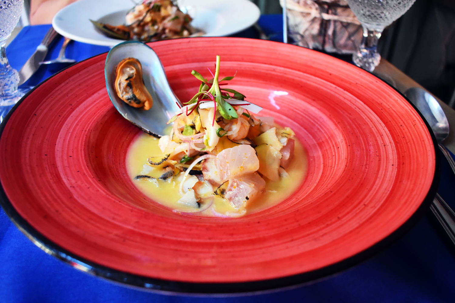 seafood dish plated on a red plate in a buttery looking sauce topped with fresh greens