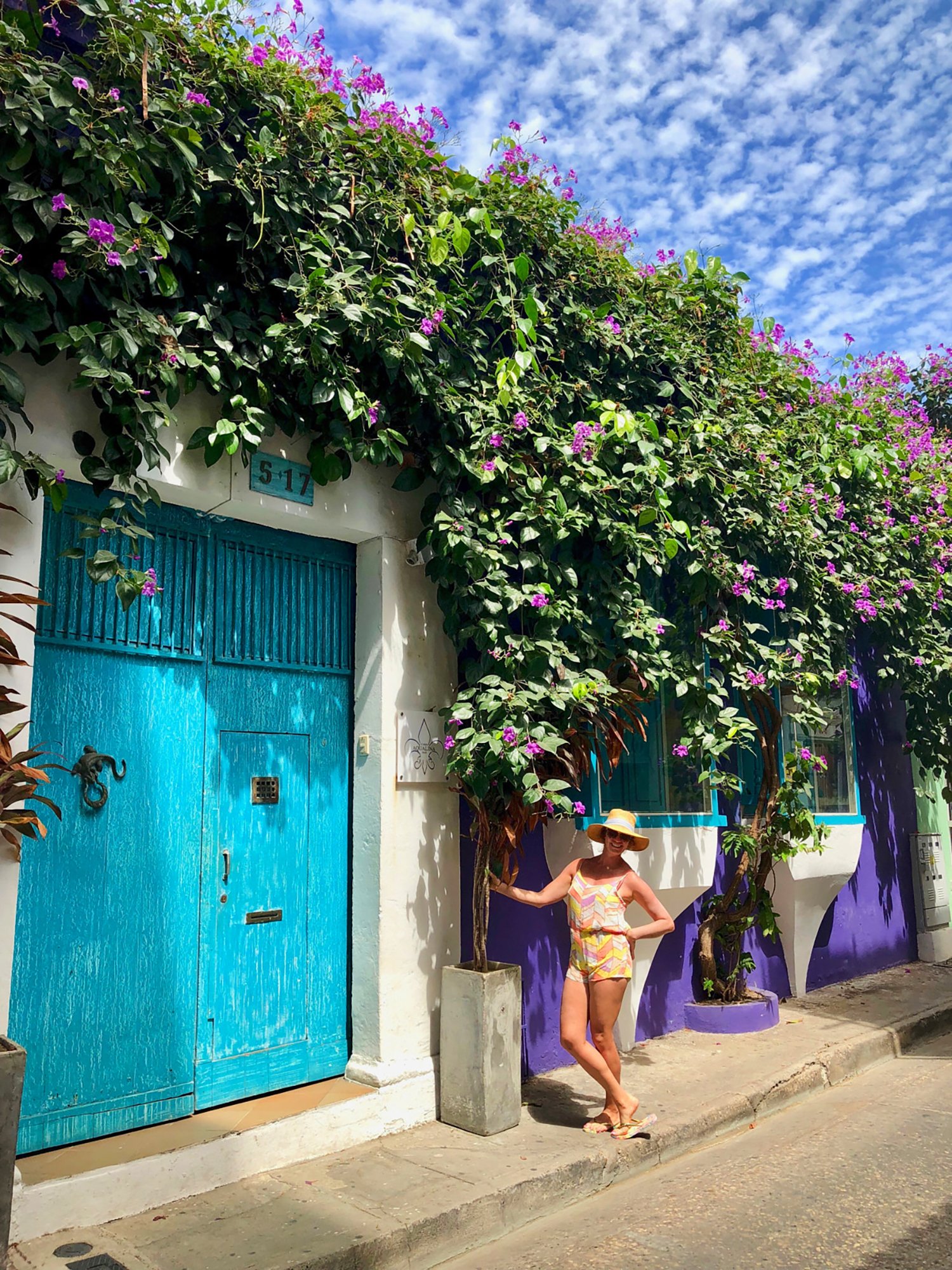 Woman standing besides a blue door against and purple wall on a colorful street in Cartagena, Colombia.