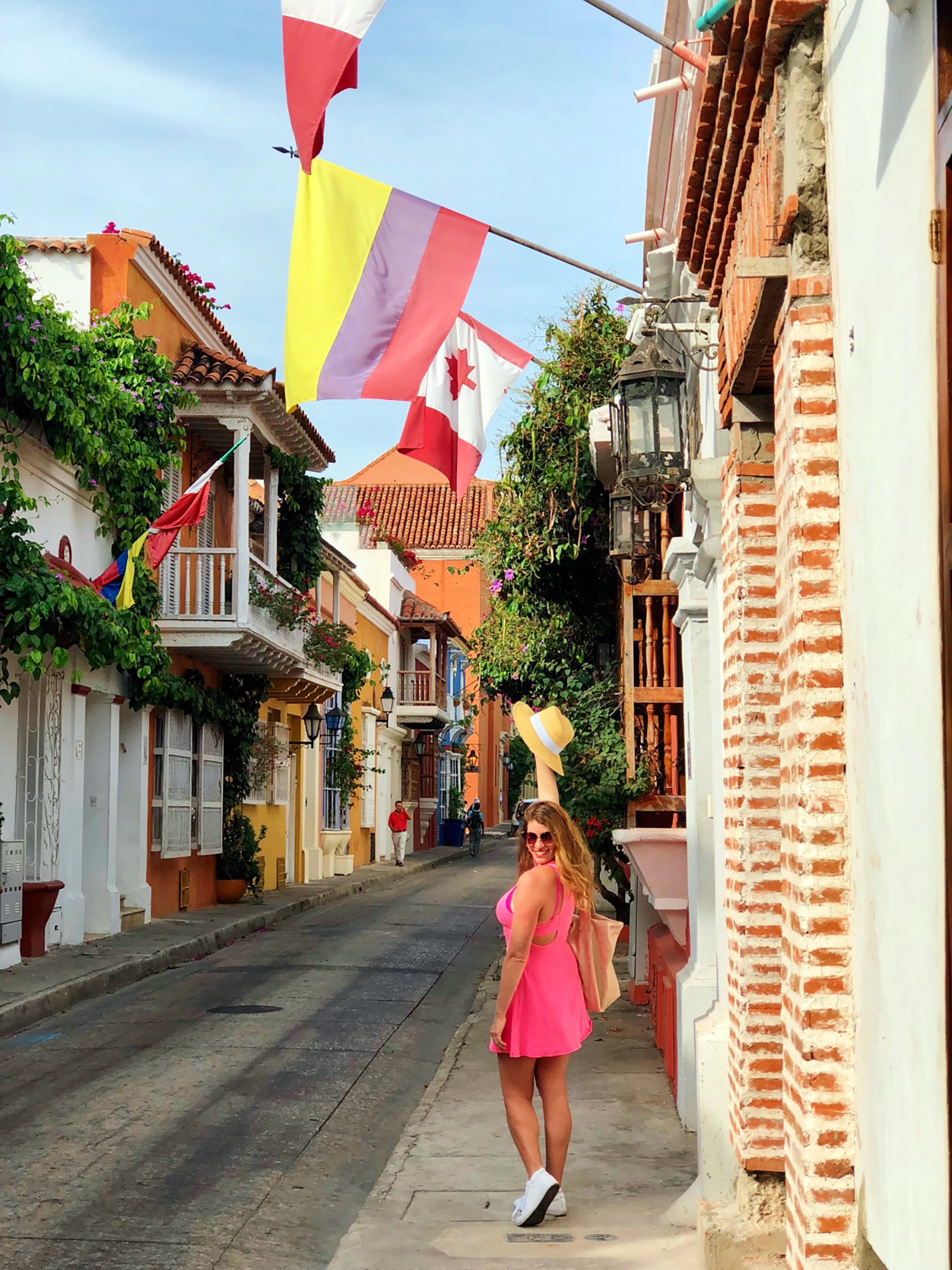 woman stanging under flags in a colorful town wearing a pink sundress and white sneakers