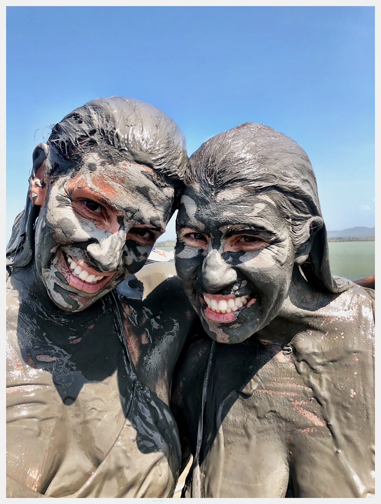 two women covered in mud posing for a photo and smiling