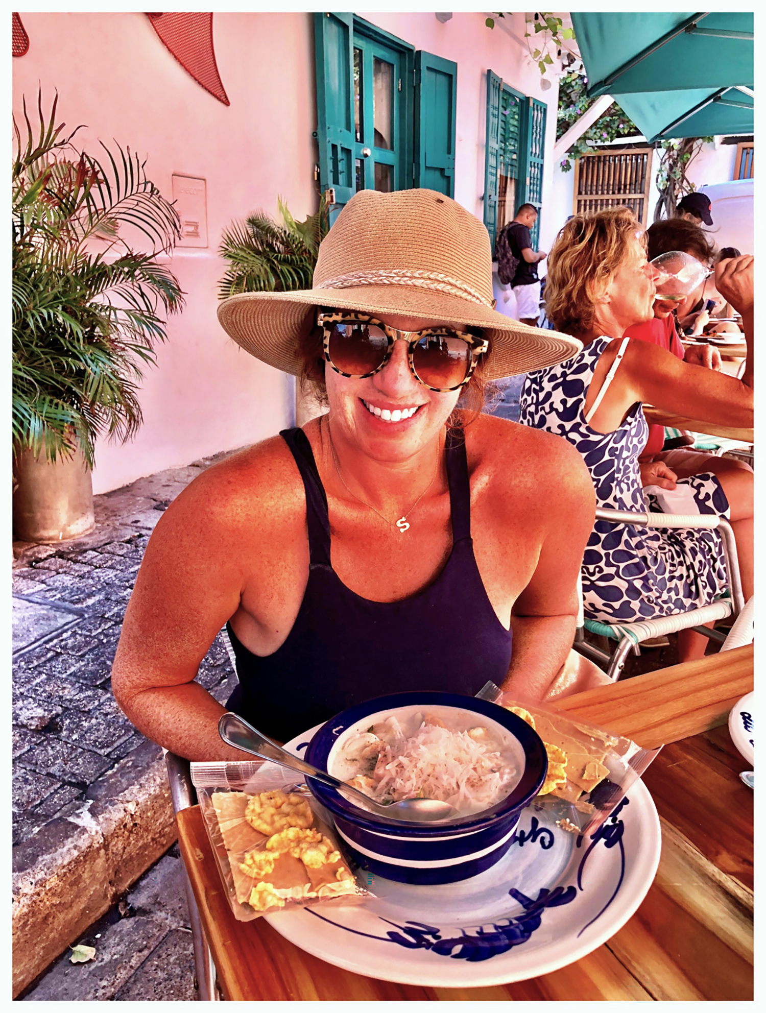 A woman in a hat and sunglasses eating soup and crackers in a cafe