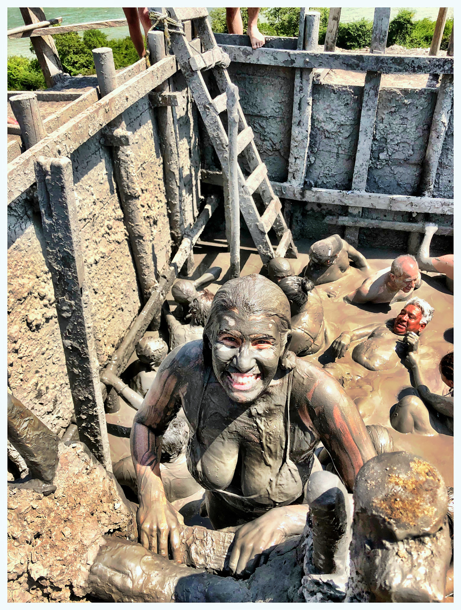 A woman in a bathing suit covered in mud climbing a latter