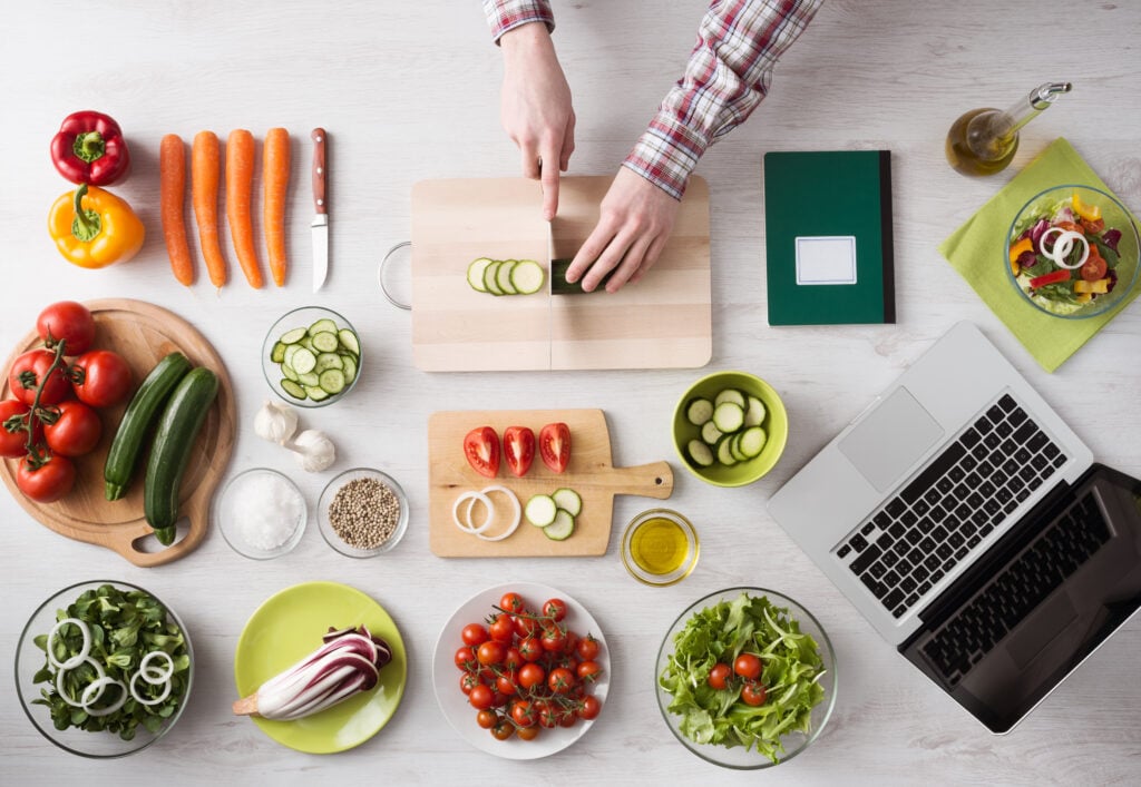 Person cutting cucumbers on a wooden cutting board with a neatly organized workstation.