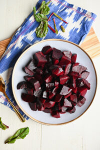 Finished beauty plate of roasted beets with an ikat blue napkin, wooden serving board, and beet greens.