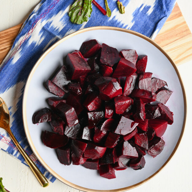 Finished beauty plate of roasted beets with an ikat blue napkin, wooden serving board, and beet greens.