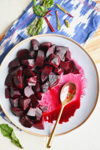 Overhead shot of a half-eaten plate of roasted beets with a gold spoon on a blue ikat napkin and wooden serving board.