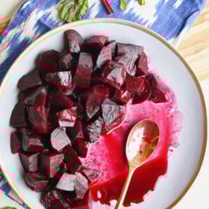 Overhead shot of a half-eaten plate of roasted beets with a gold spoon on a blue ikat napkin and wooden serving board.
