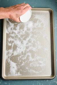 Hand sprinkling kosher salt on a sheet tray.