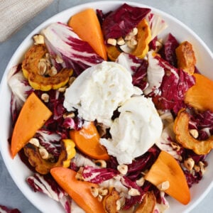 Close-up shot of plated persimmon salad with beige linen, Delicata squash, and toasted hazelnuts.