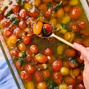 Hand holding a gold spoon of finished tomato confit drizzled with balsamic glaze, styled with pink and blue linens.