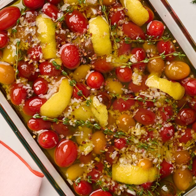 Close-up shot of uncooked tomato confit with fresh tomatoes, olive oil, garlic, shallots, lemon peel, and thyme, ready to go into the oven.