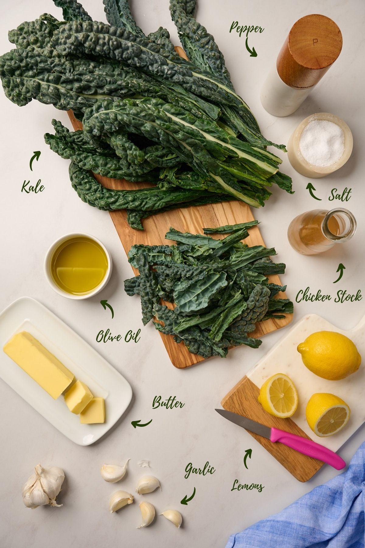 Ingredients for making sautéed kale including fresh kale, olive oil, garlic, chicken stock, butter, lemon, salt, and black pepper.