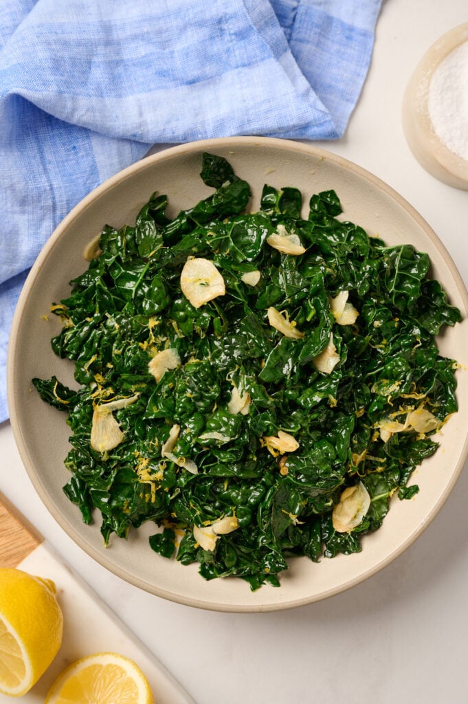 Overhead view of a finished bowl of sautéed kale on a table with blue linen
