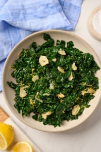 Overhead view of a finished bowl of sautéed kale on a table with blue linen