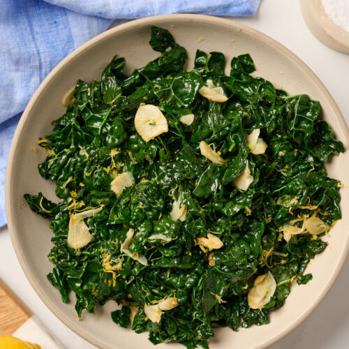 Overhead view of a finished bowl of sautéed kale on a table with blue linen