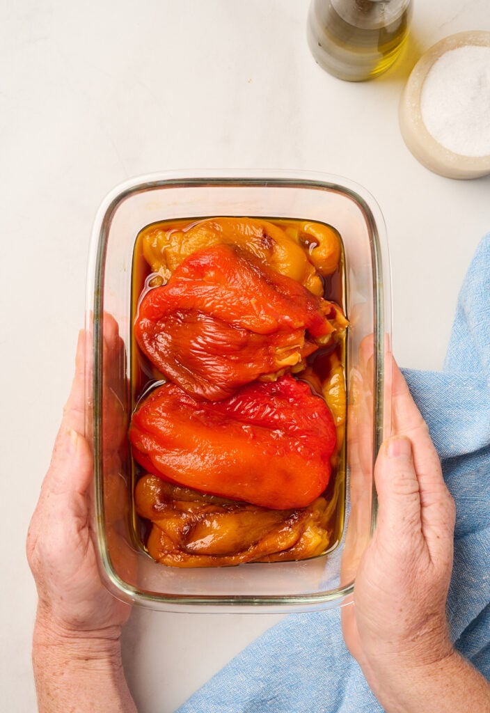 Hands holding a container filled with peeled, roasted bell peppers