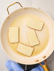 Thick slices of Kefalograviera cheese searing in olive oil in a skillet