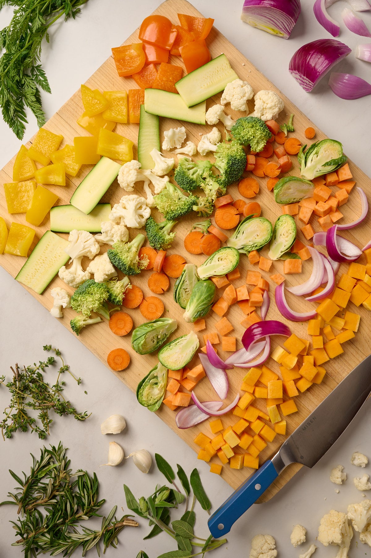 Chopped vegetables arranged on a wooden cutting board with olive oil and herbs in the background