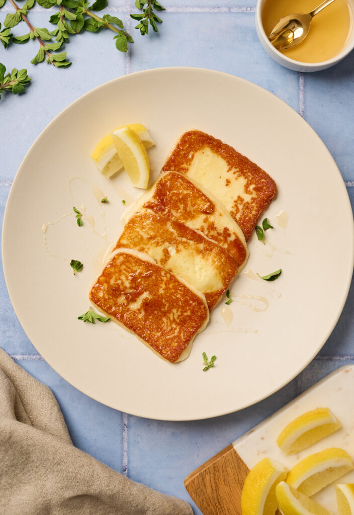 Crisped Greek cheese plated with a drizzle of honey and lemon wedges on a blue tile background