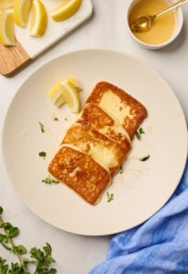 Pan-fried saganaki cheese served on a plate with honey drizzle and lemon wedges on white marble