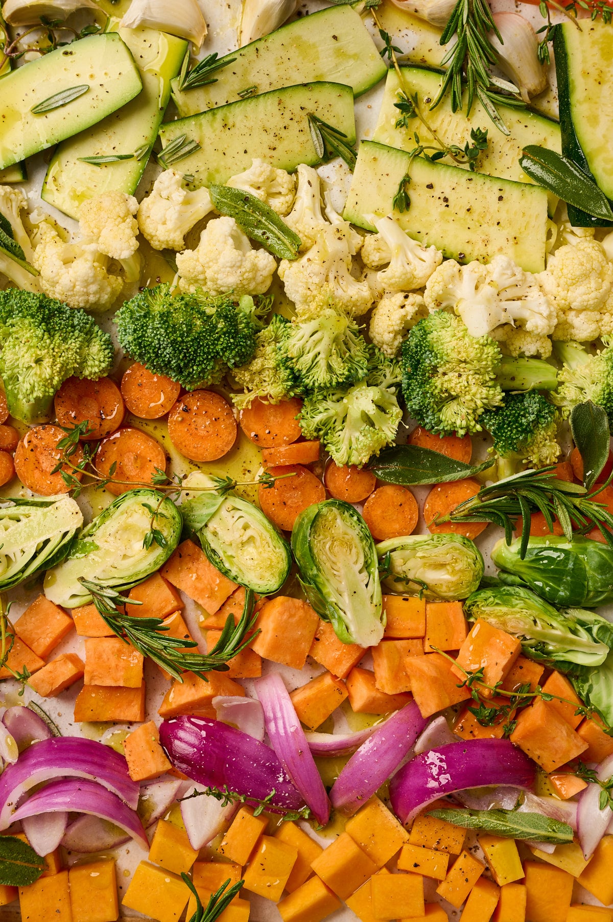 Close-up of raw vegetables on a sheet pan coated with olive oil, salt, and pepper