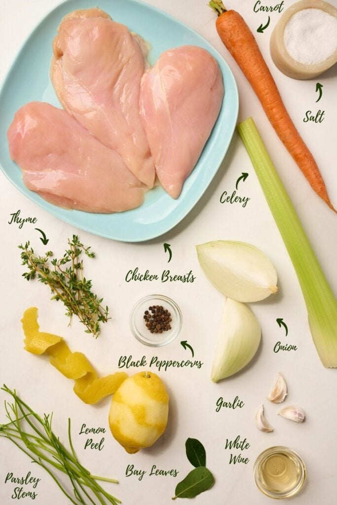 : Ingredients for making poached chicken including boneless breasts, aromatics, herbs, and white wine