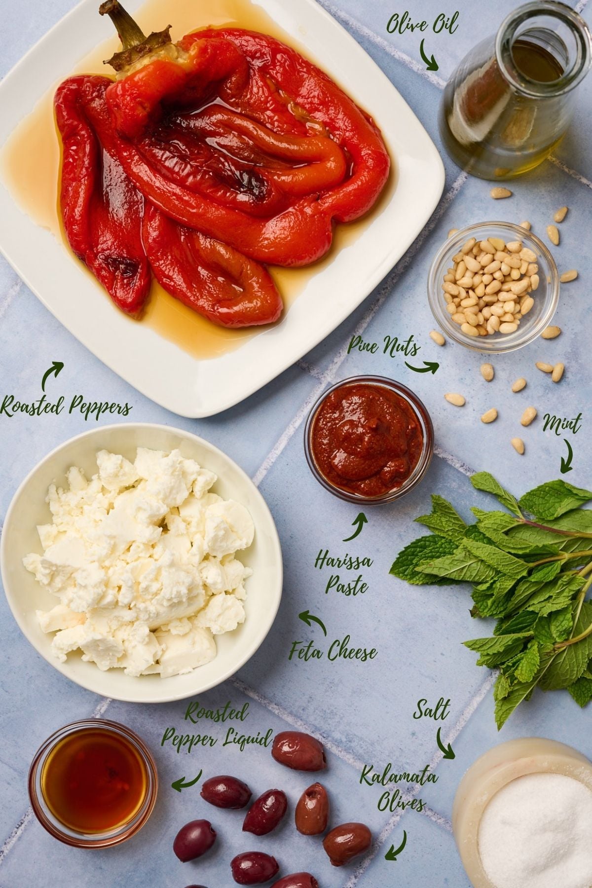Overhead shot of tirokafteri dip ingredients including feta, roasted pepper, olive oil, harissa, and mint