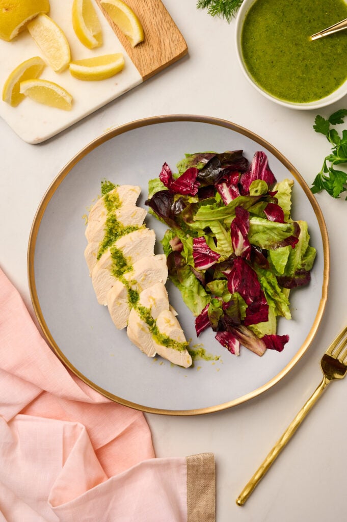 Plate of sliced poached chicken topped with herb vinaigrette and fresh salad
