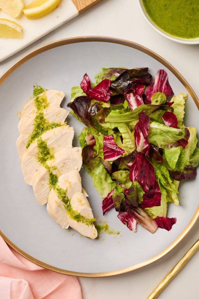 : Close-up view of sliced poached chicken with vinaigrette and salad on a ceramic plate