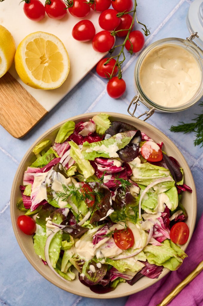 Large salad drizzled with tahini dressing, jar and ingredients in background