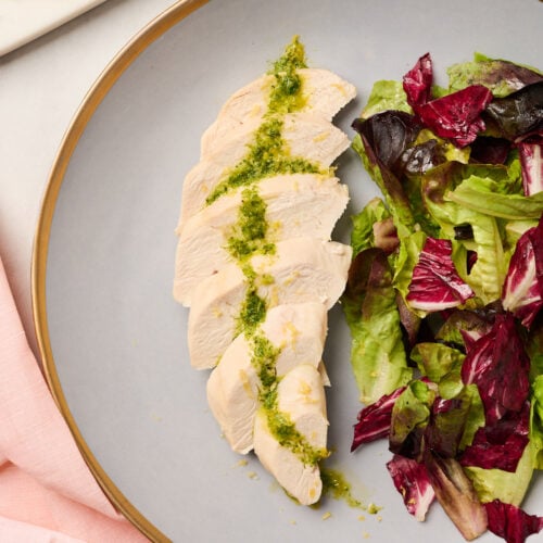 : Side angle of plated poached chicken with vinaigrette and mixed greens