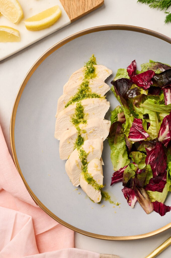 : Side angle of plated poached chicken with vinaigrette and mixed greens