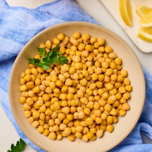 Close-up of cooked chickpeas in a bowl with lemon and cooking broth on the side