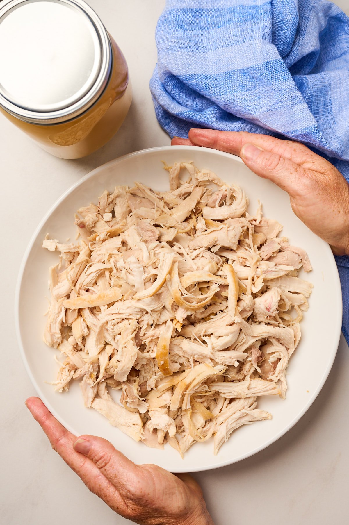Hands holding a finished bowl of freshly shredded chicken