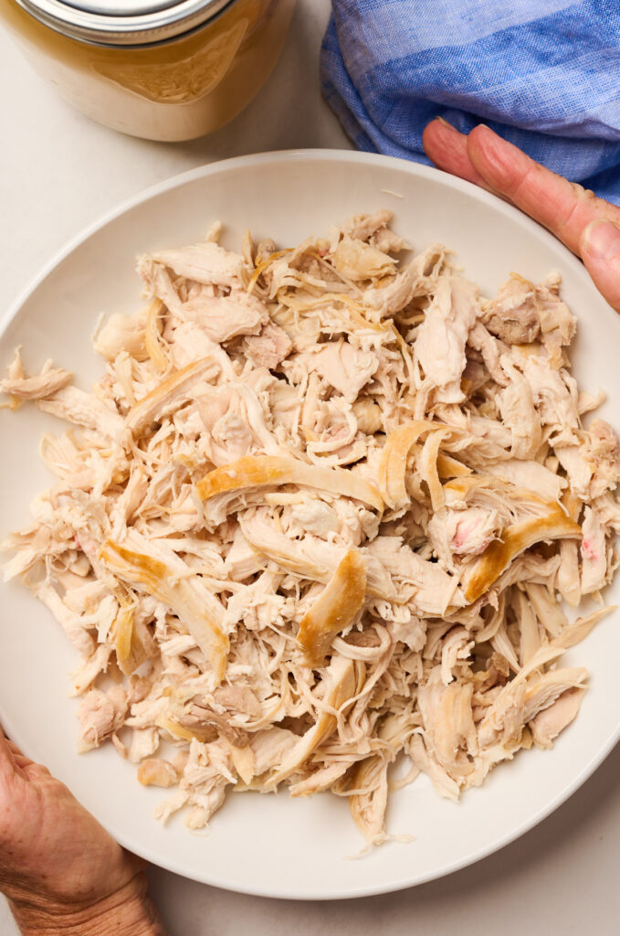 Close-up of shredded chicken held in hands in a white bowl