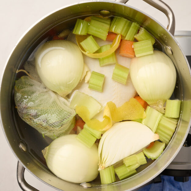 Whole chicken, vegetables, and herb bundle placed in a pot with water