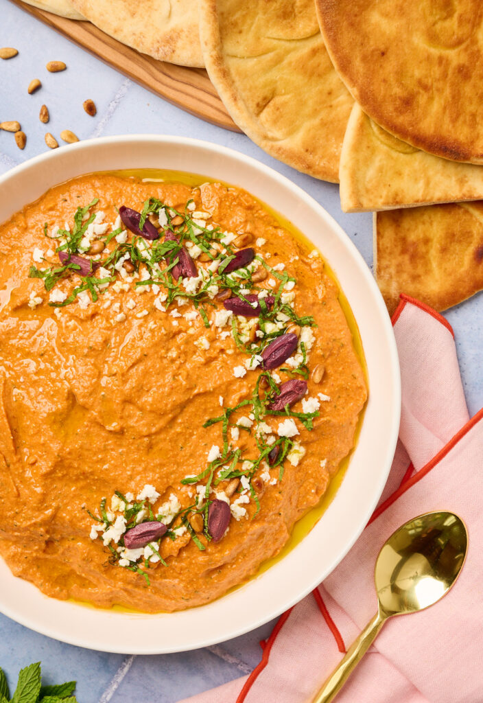 Side angle of tirokafteri served with pita and garnished with Mediterranean toppings