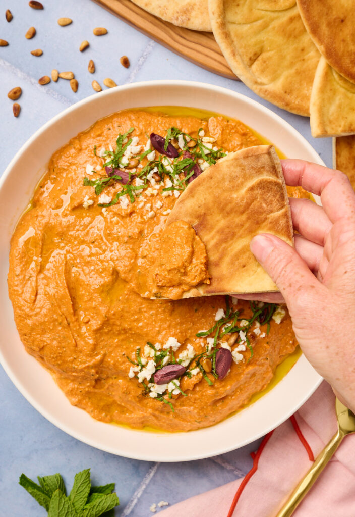 Hand dipping toasted pita into the whipped tirokafteri spread