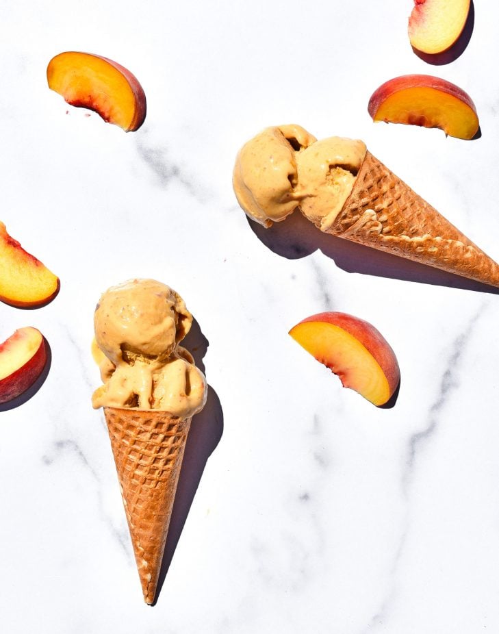 two ice cream cones filled with peach ice cream and surrounded by peach slices